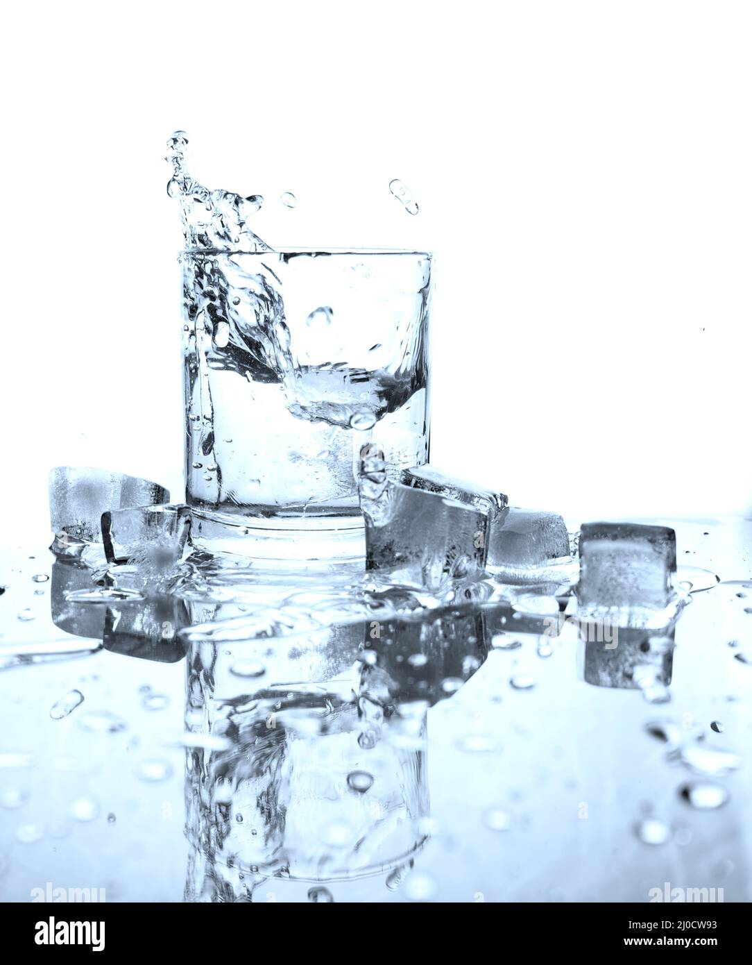 Drinking water splashed with ice in glass on white background with reflections. Stock Photo