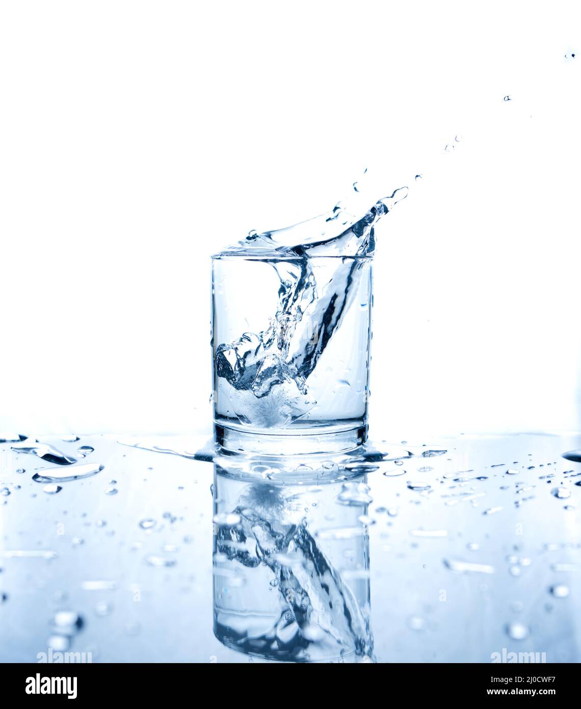 Drinking water splashed with ice in glass on white background with reflections. Stock Photo
