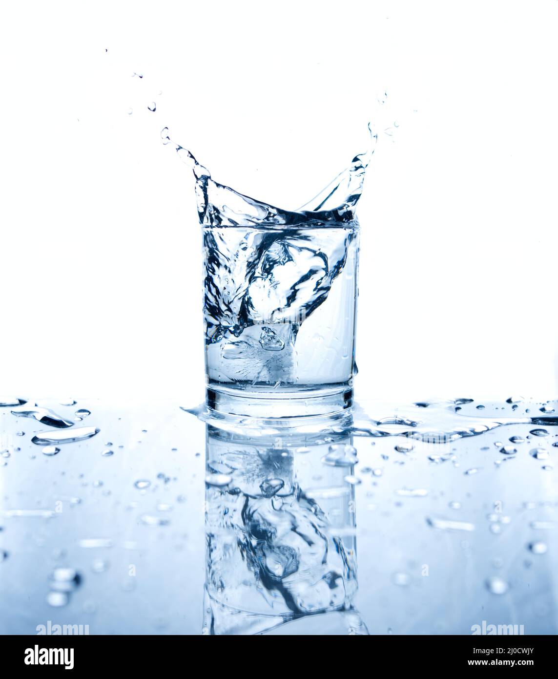 Drinking water splashed with ice in glass on white background with reflections. Stock Photo