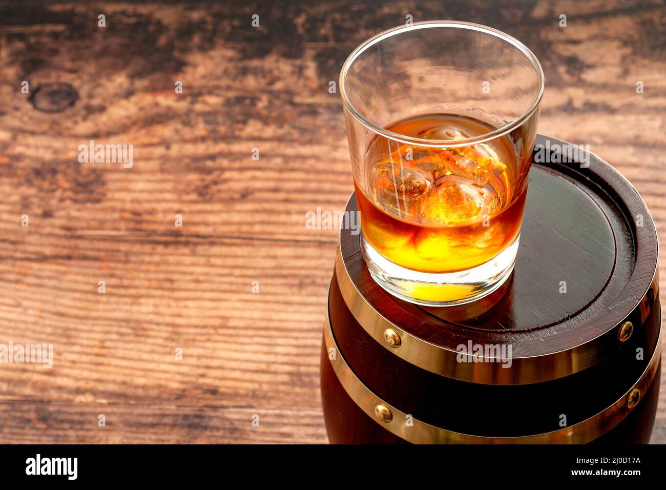 Strong spirit, masculine or macho lifestyle and whisky distillery concept with glass of good bourbon on the rocks and oak barrel on the cellar wooden Stock Photo