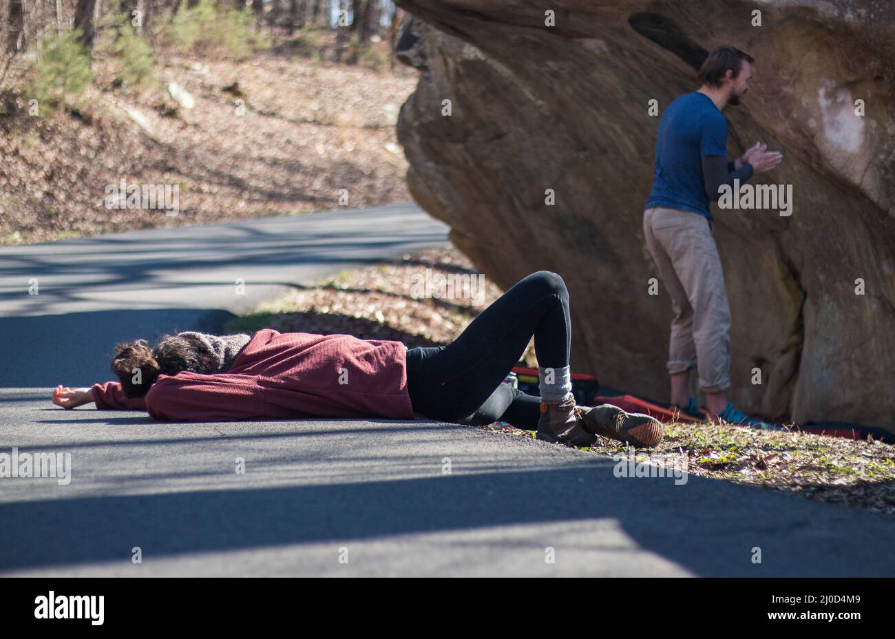 Outdoorsy woman lying on road outdoors films rock climber starting a climb Stock Photo