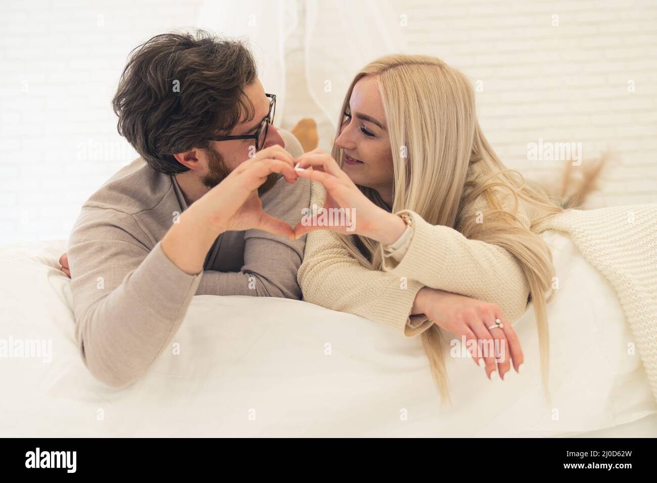 adorable young couple lying on the bed making a heart shape together with their hands. High quality photo Stock Photo