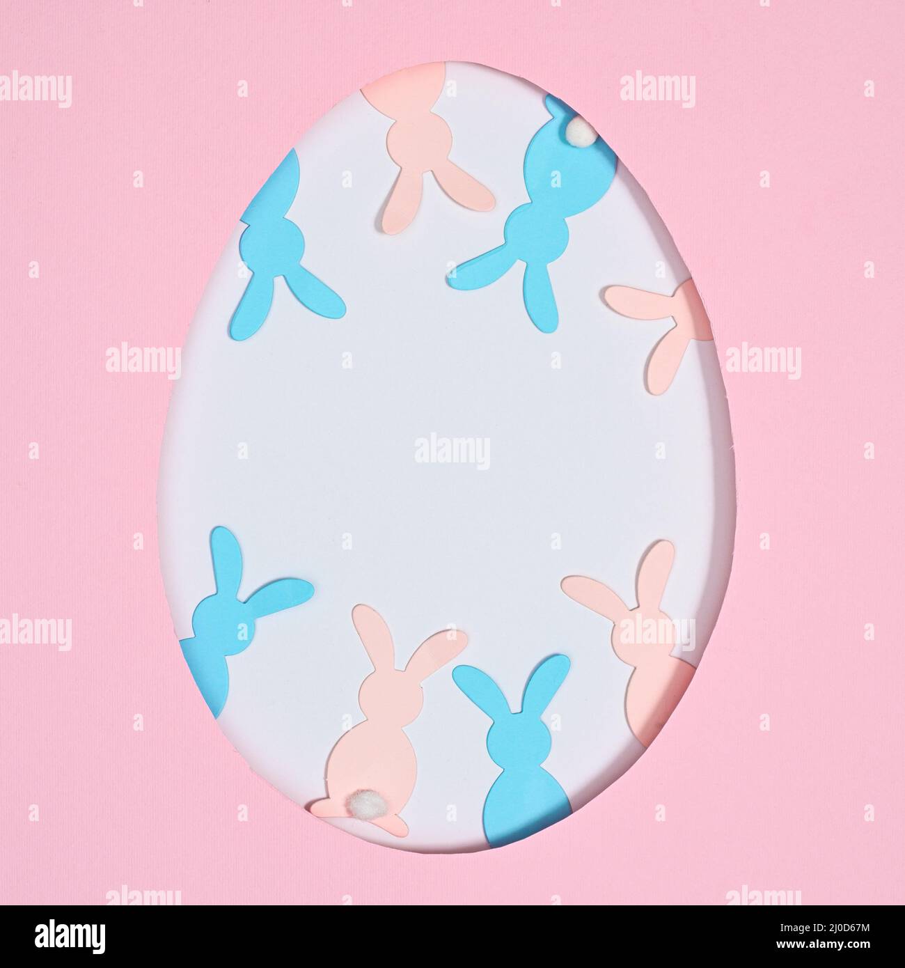 Easter egg shape frame with pastel pink and blue rabbits on pastel pink ...