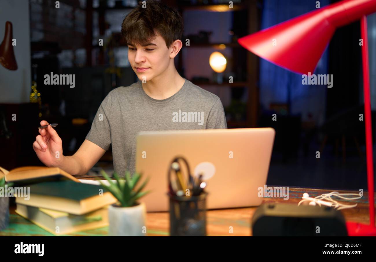 Teenage student learning at home with books and laptop computer. Online school and education, sitting at desk. Stock Photo