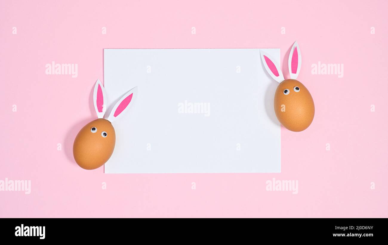 Two natural eggs with bunny ears and eyes on pastel pink background ...