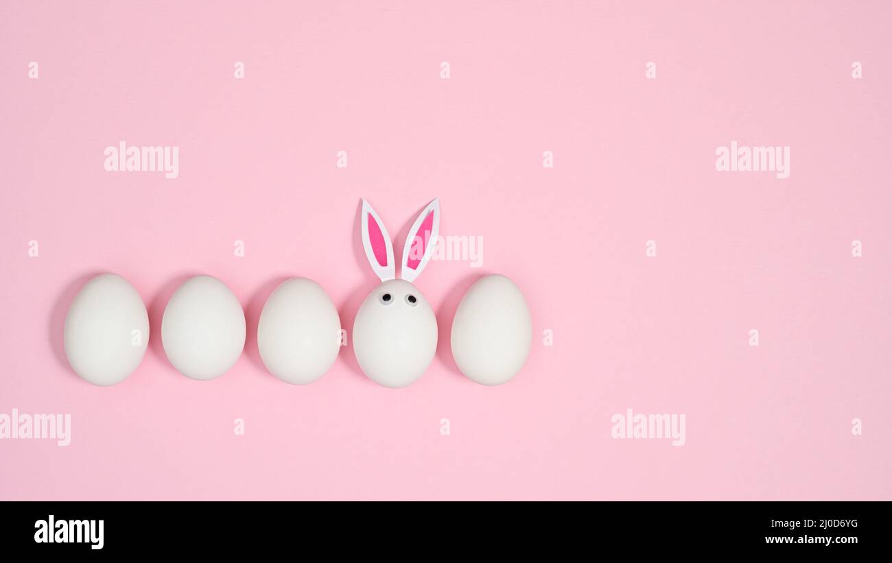 Creative composition with white eggs and one with rabbit ears on pastel pink background. FLat lay creative Easter copy space. Stock Photo
