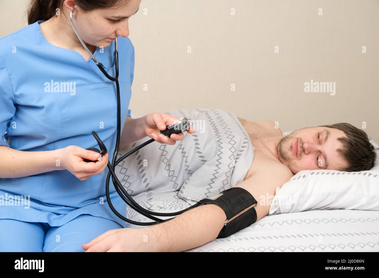 The doctor measures the blood pressure of a young 30-year-old man lying in bed. Diseases of the heart and blood vessels in humans, mechanical Stock Photo