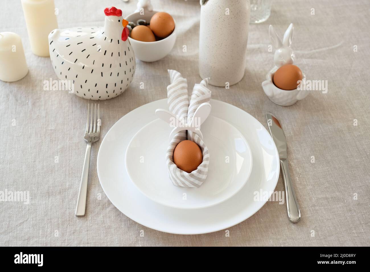 Cute Easter table setting. Easter egg in Easter bunny napkin on plate on linen tablecloth. Stock Photo