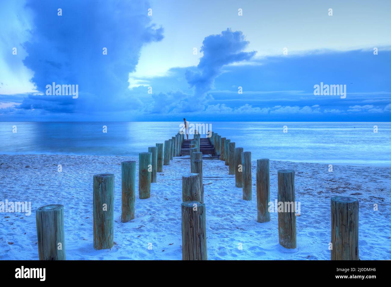 Fisherman stands on an old pier at the ocean on Naples Beach Stock Photo