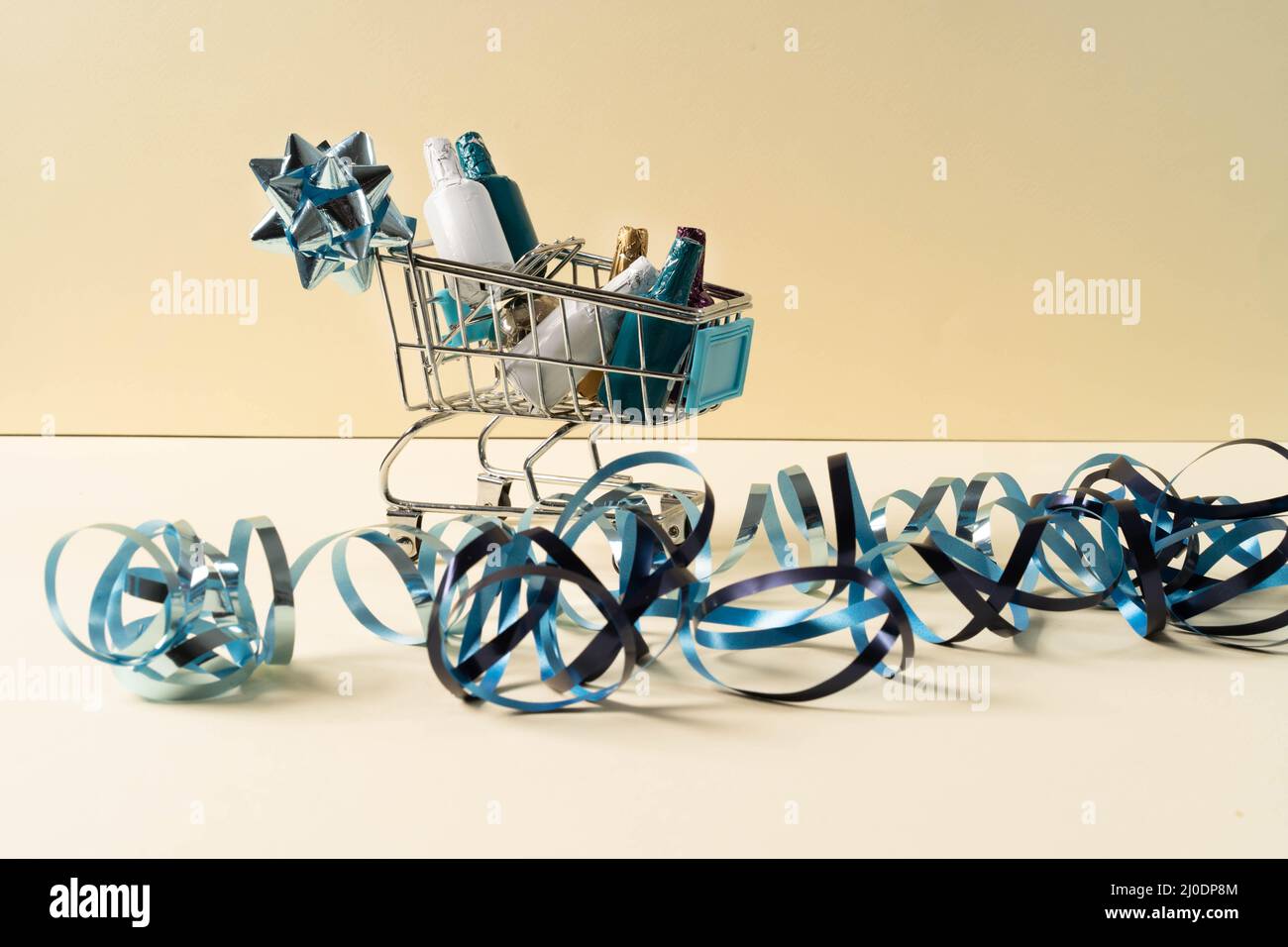 A small shopping cart with bottles of alcohol and confetti. The concept of a holiday, online shopping, sales and preparation for a wedding, birthday. Stock Photo