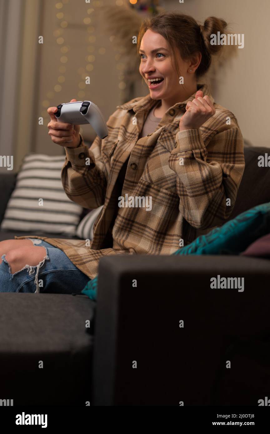 Teen girl playing with friends in a virtual adventure video game at home, in the room. She has a gamepad in her hands. Virtual reality, gaming, prizes Stock Photo