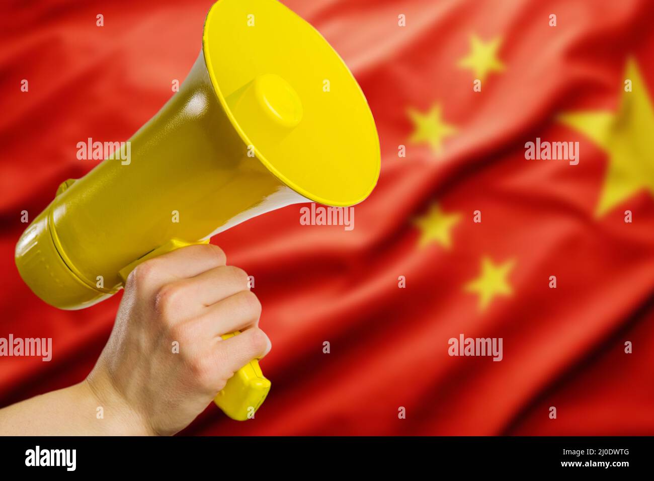 National Chinese flag and a yellow horn in a man's hand. Speaker, rumors, fakes, information, demonstrations, elections, speaker. Banner. Stock Photo