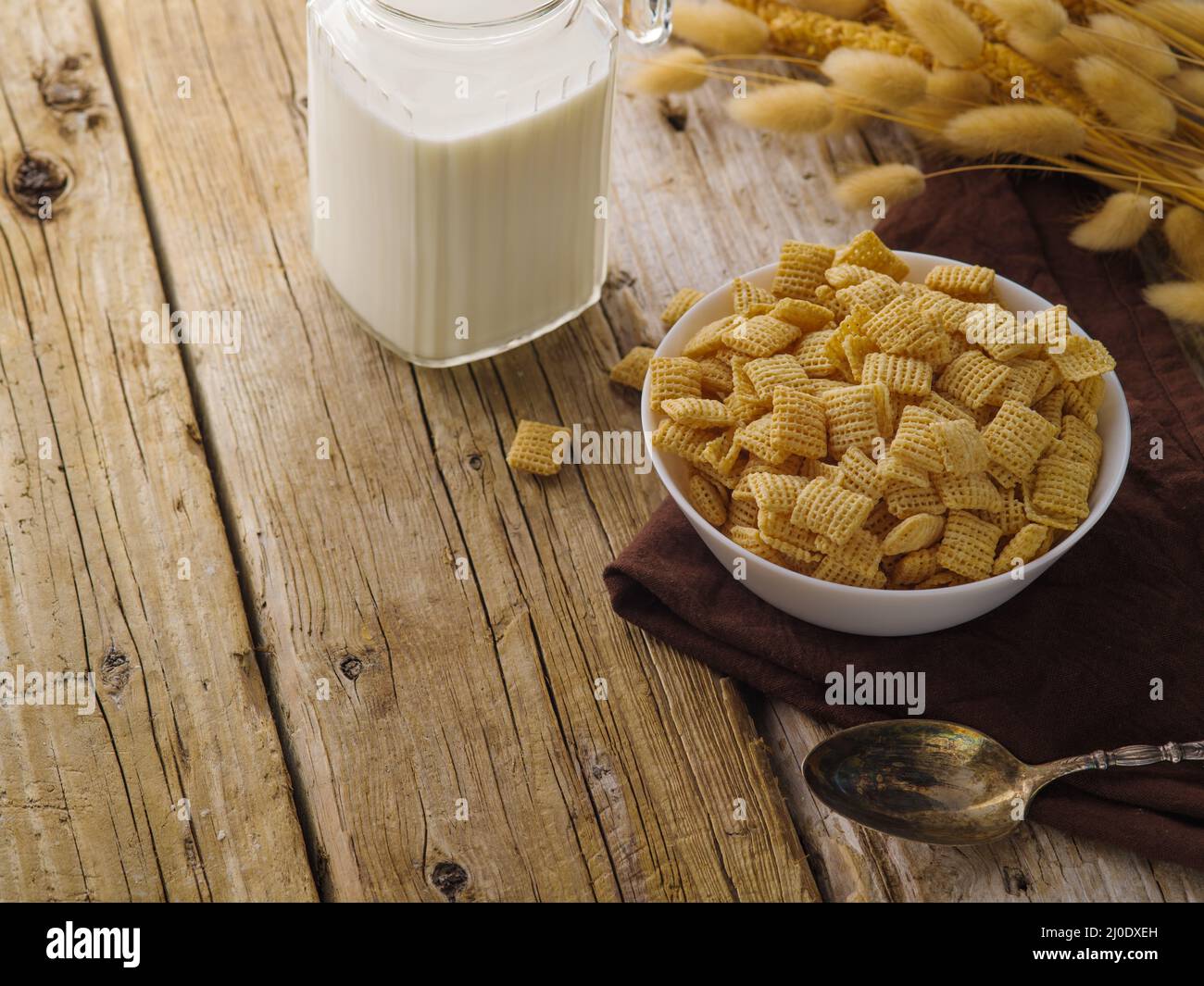 Whole grain crunchy pads, milk in a jug and a bunch of cereals on a wooden table. Country style. Traditional american breakfast, healthy lifestyle, or Stock Photo