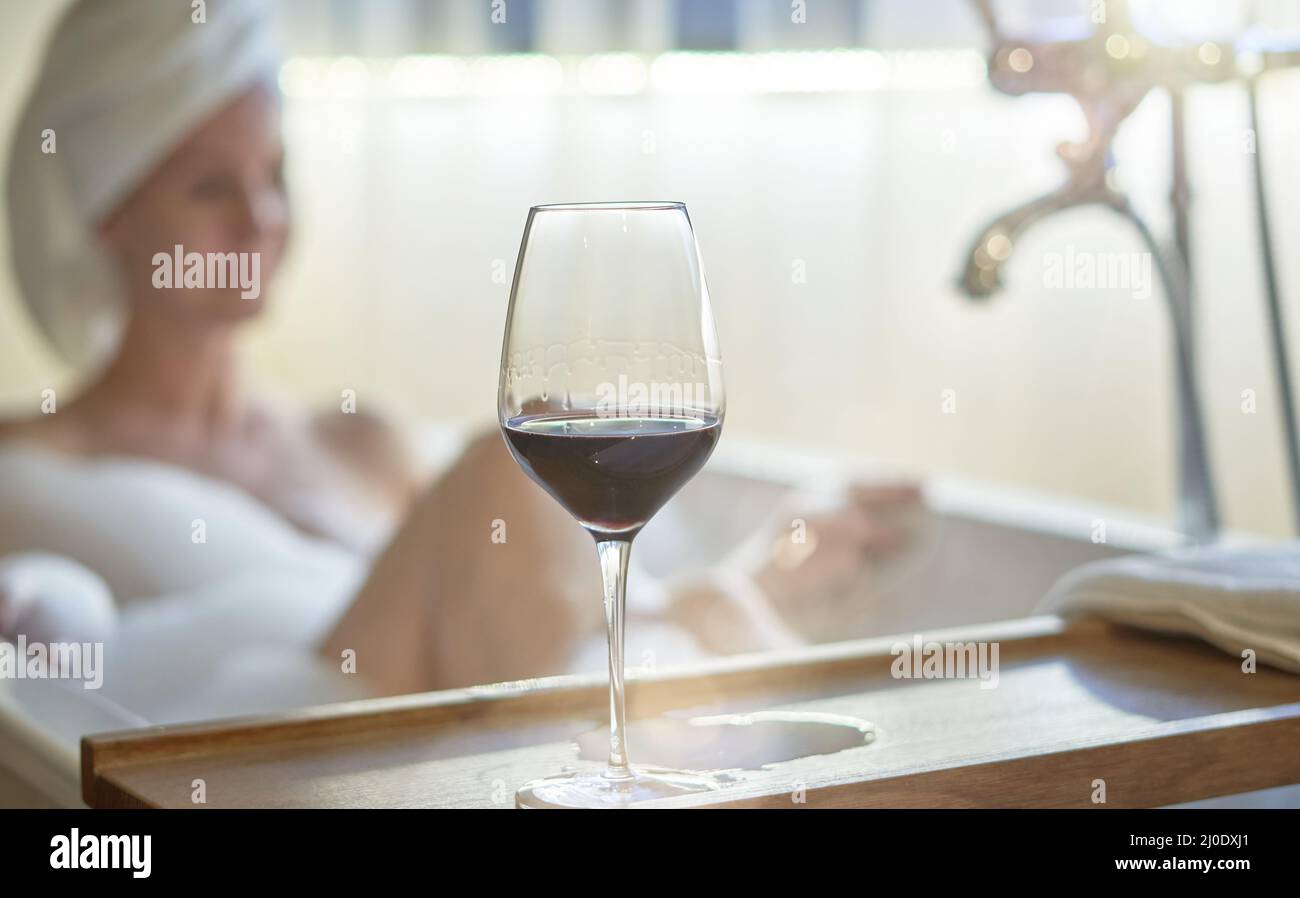 Woman relaxing in bubble bath in bathtub drinking tasting red wine