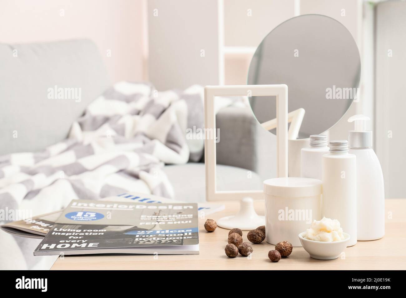 Bowl of shea butter, nuts, cosmetic products and magazines on table in room Stock Photo