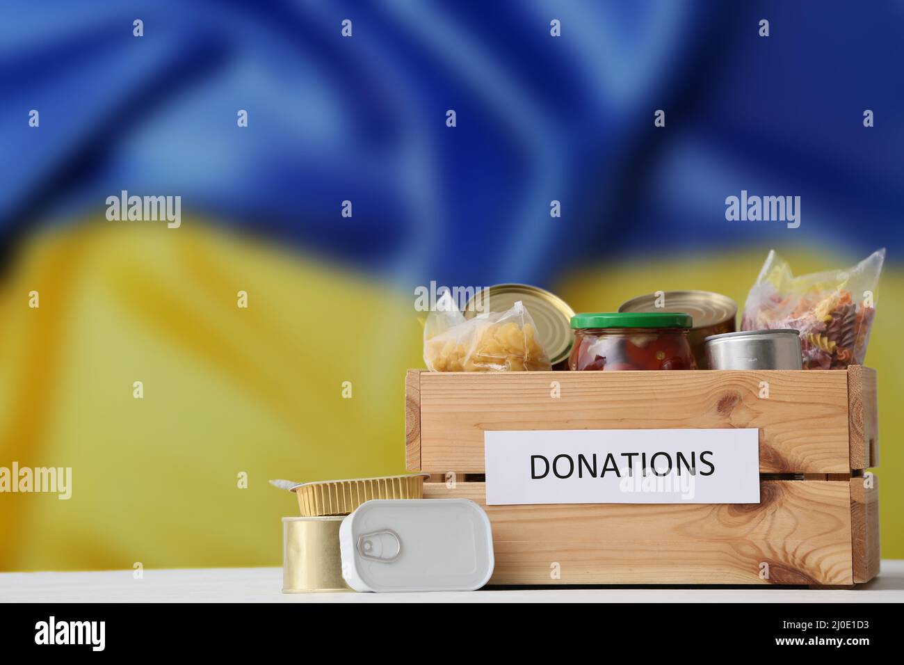 Donation box with products against Ukrainian flag. Humanitarian assistance for Ukraine Stock Photo