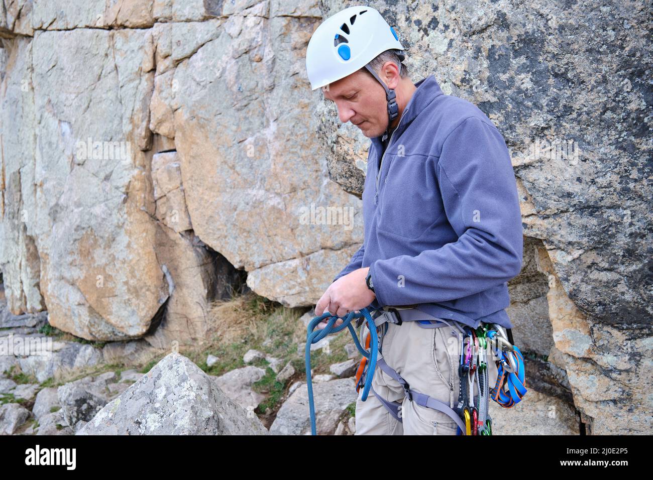 A Rock climber wearing safety harness making a rope knot Stock Photo