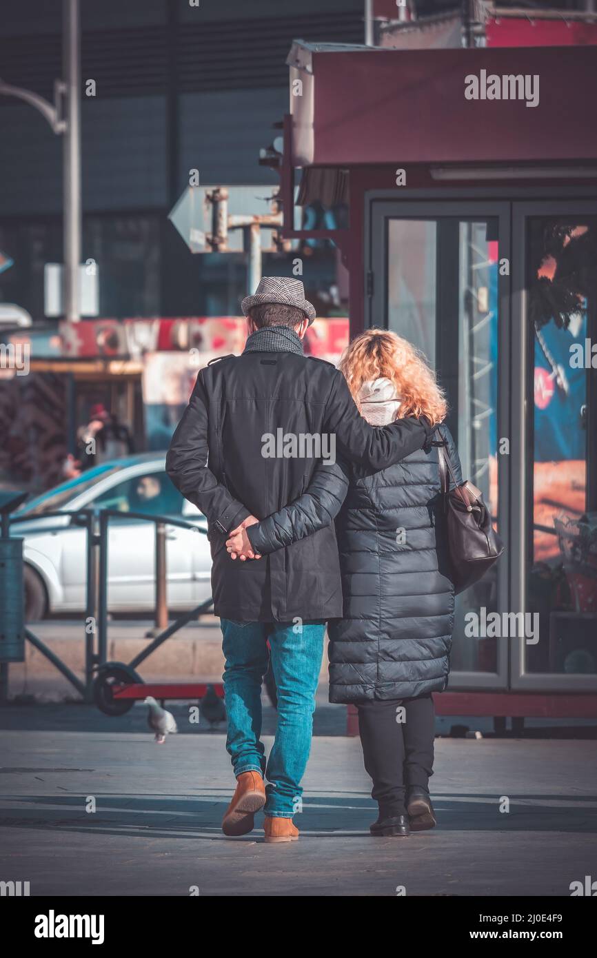 rear view with a couple holding hands and walking on the sidewalk in ...