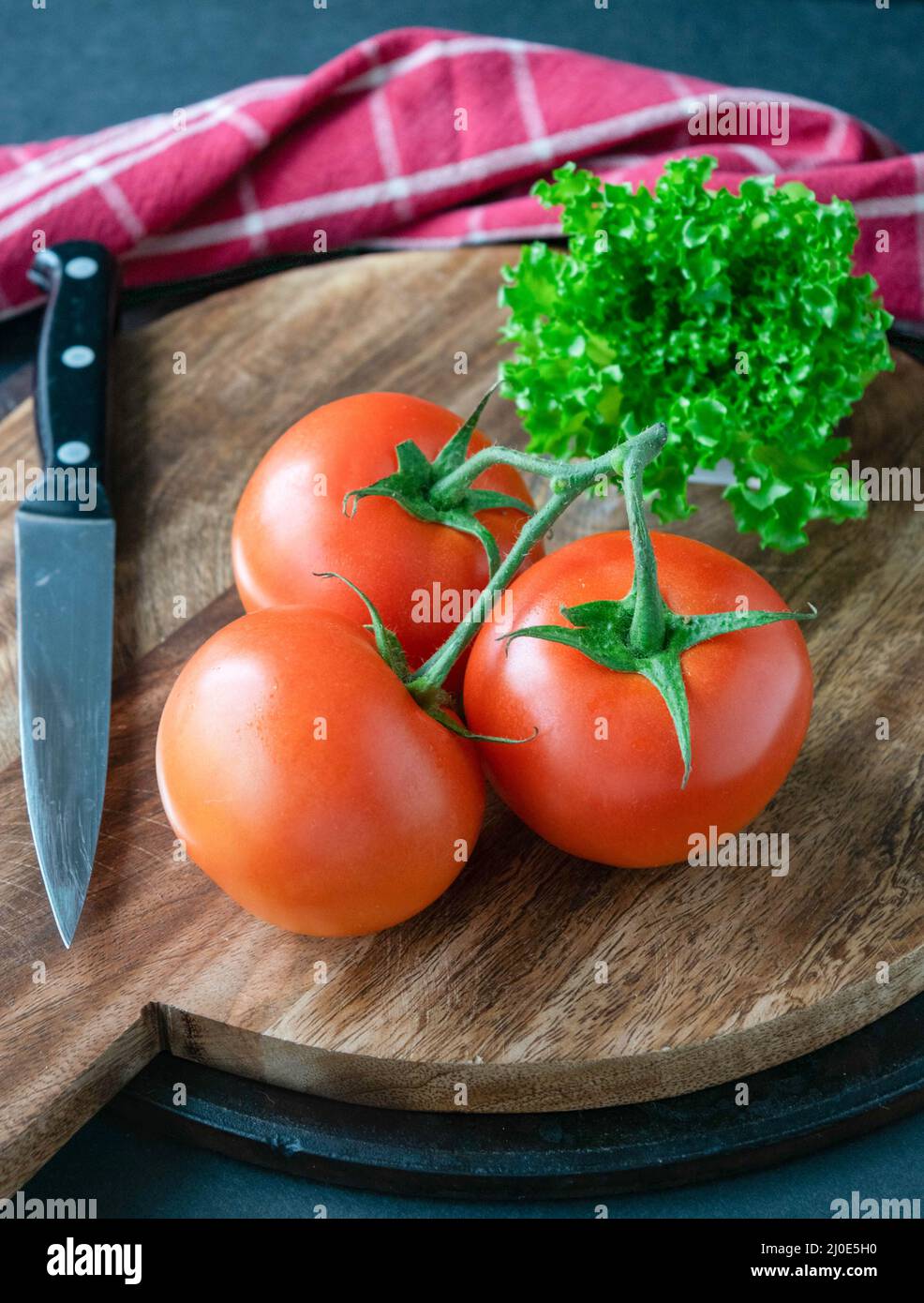 3 red tomatoes and a bunch of green lettuce on a round, wooden cutting ...