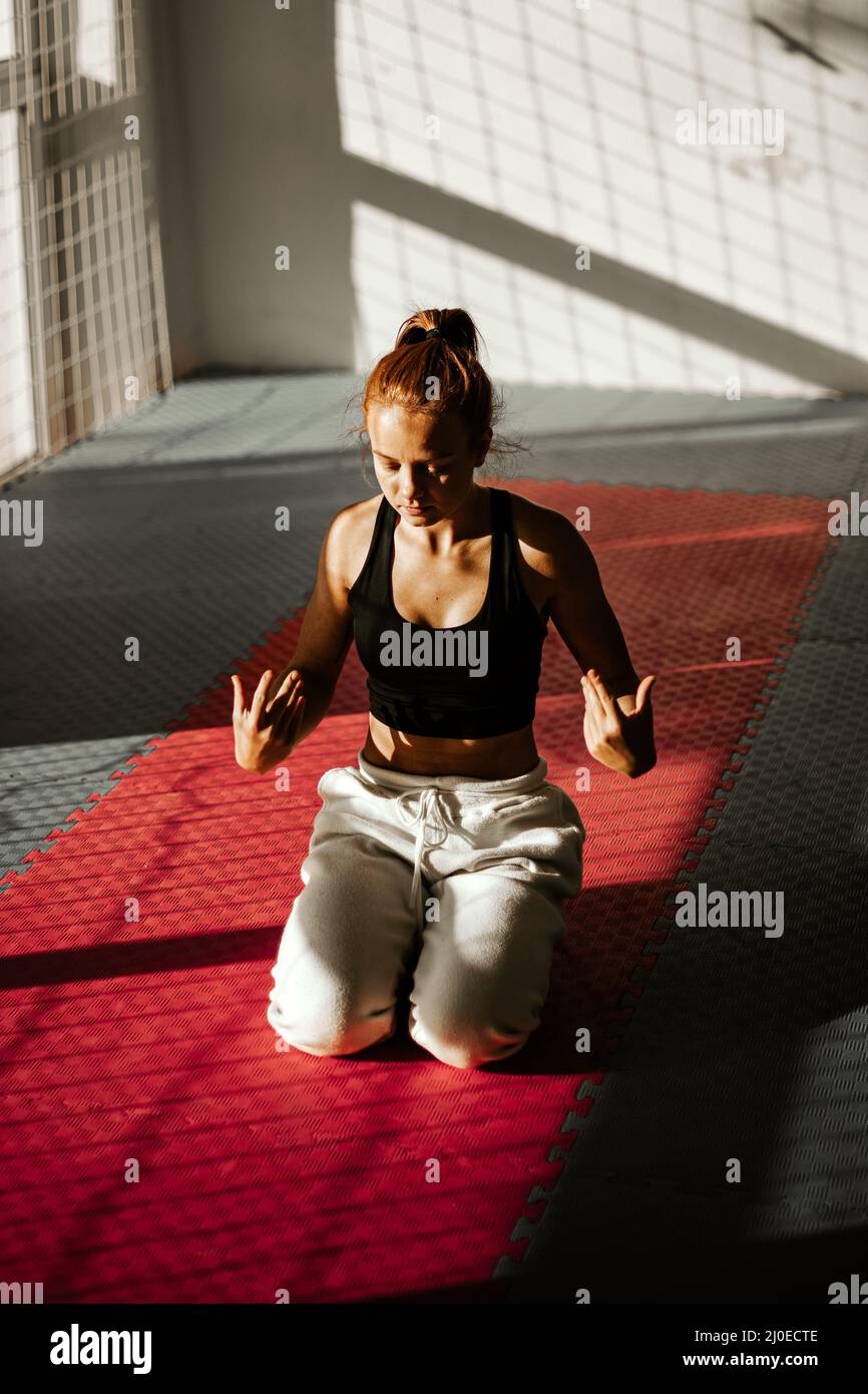 woman kneels and shakes hands. woman's hands hurt while exercising. sunset in the gym.  Stock Photo