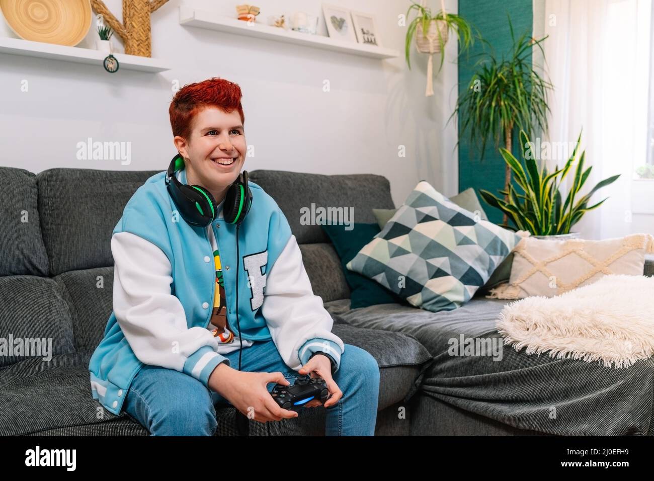 Non-binary smiling person playing video games in the living room at home Stock Photo