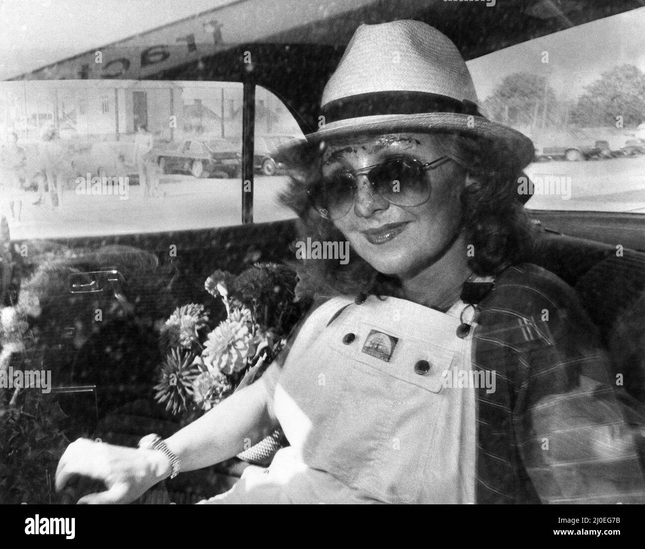 Singer Lulu in the back of a car wearing a trilby hat, sunglasses and dungarees, with a large bunch of flowers.   September 1979 P035550 Stock Photo