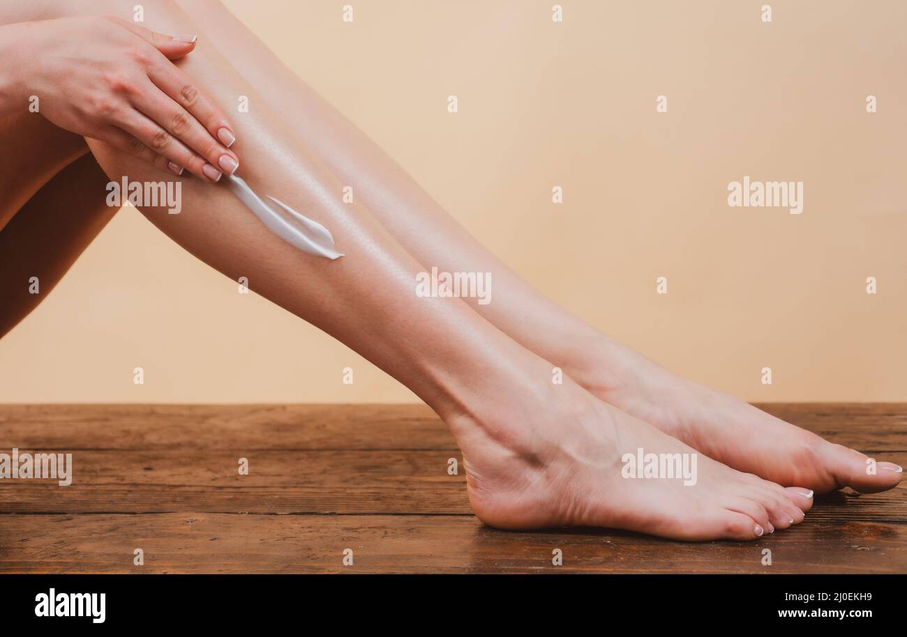Young woman applying body lotion on legs. Cosmetic cream on woman leg