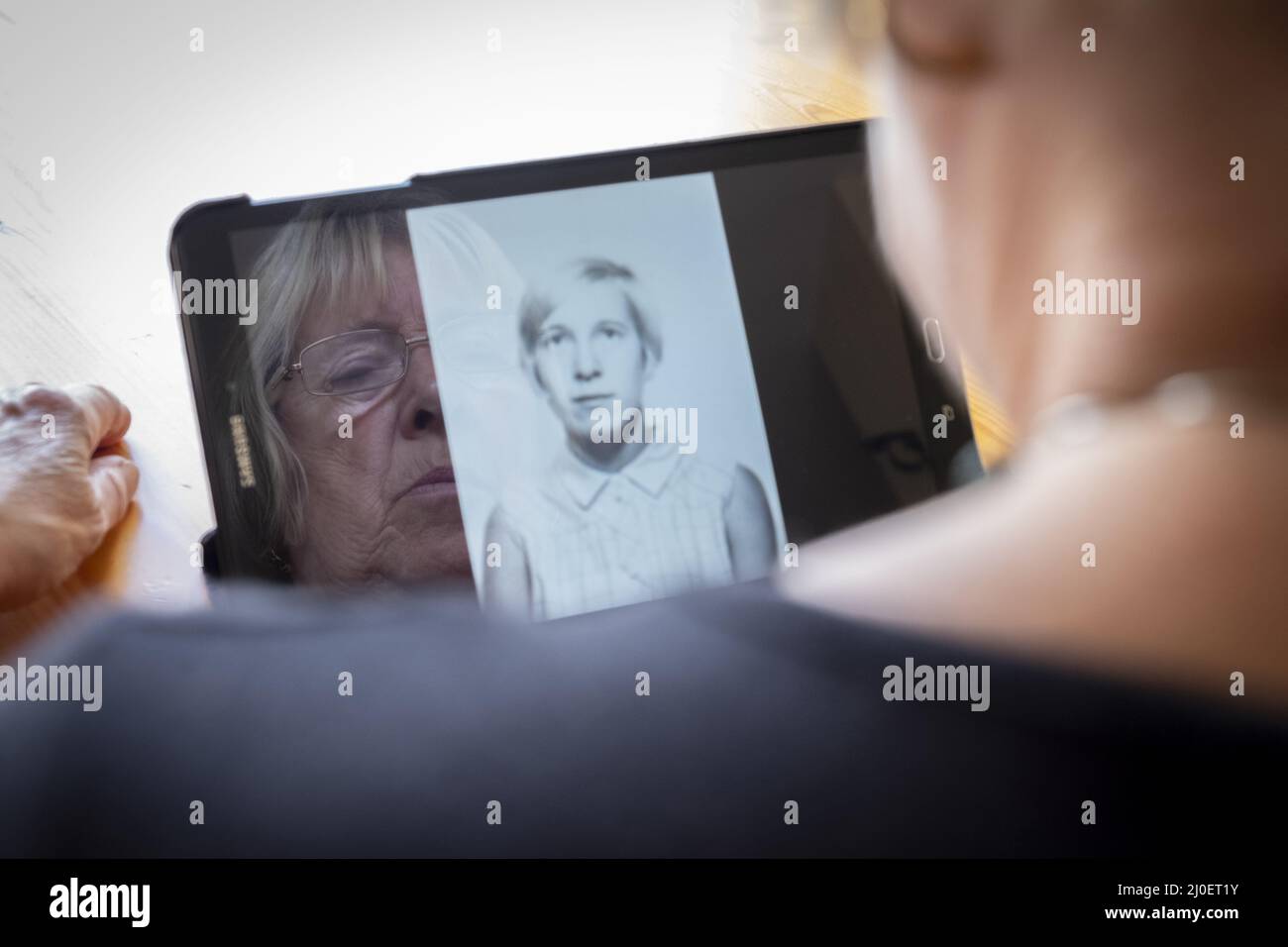 Senior caucasian woman looking at old photos of herself as a young woman on a tablet computer Stock Photo
