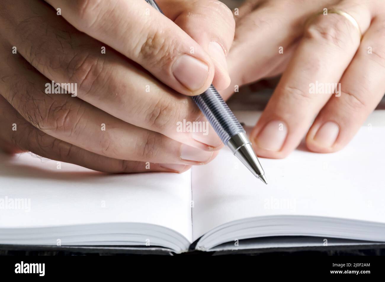 The right hand of a man writing with a pen on a notebook with blank pages. Stock Photo