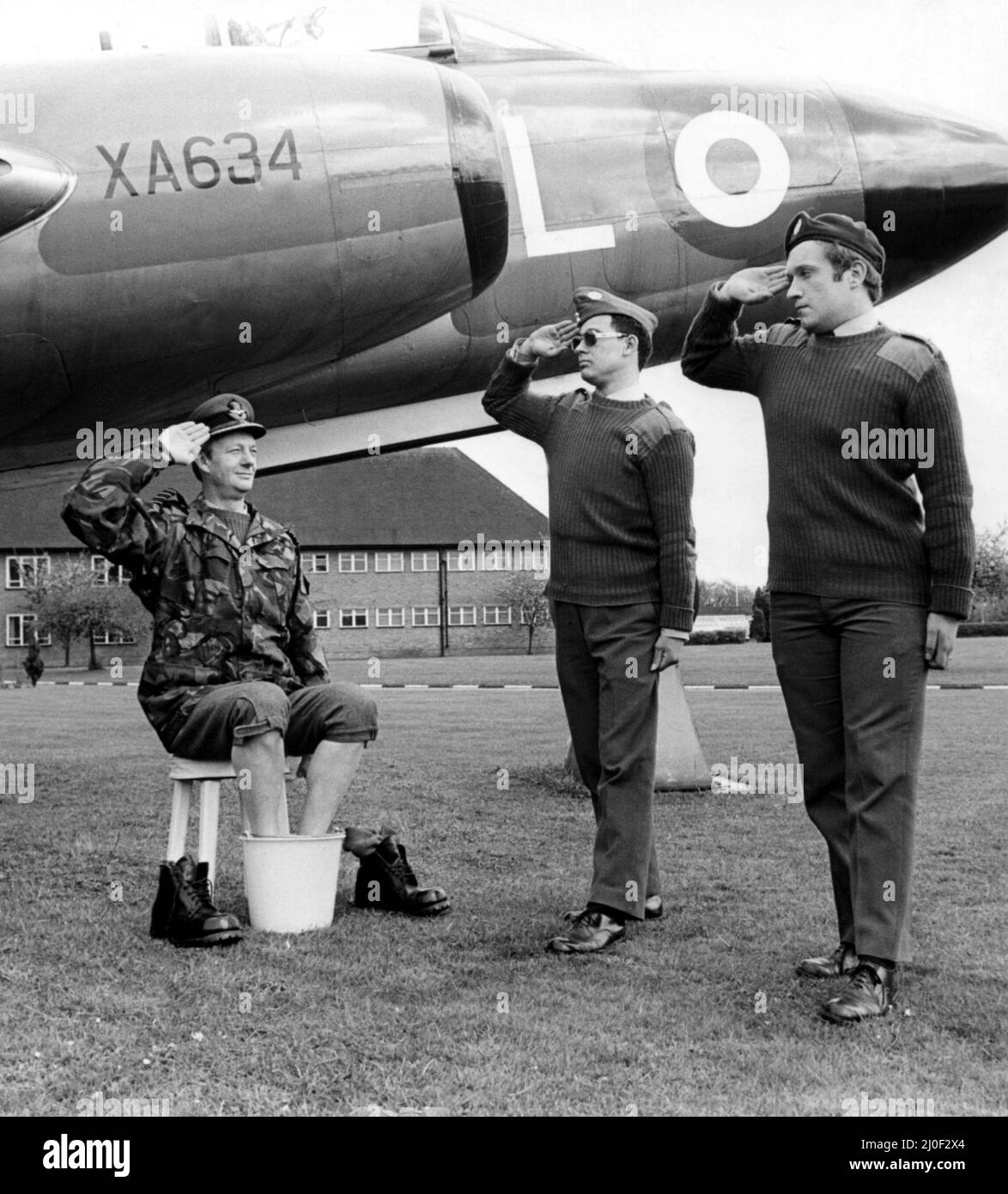 A picture from a series of humurous novelty images taken by Sunday People photographer Dennis Hutchinson - An officer soaking his feet under a Gloster Javelin receives a salute.   Circa: 1980 Stock Photo