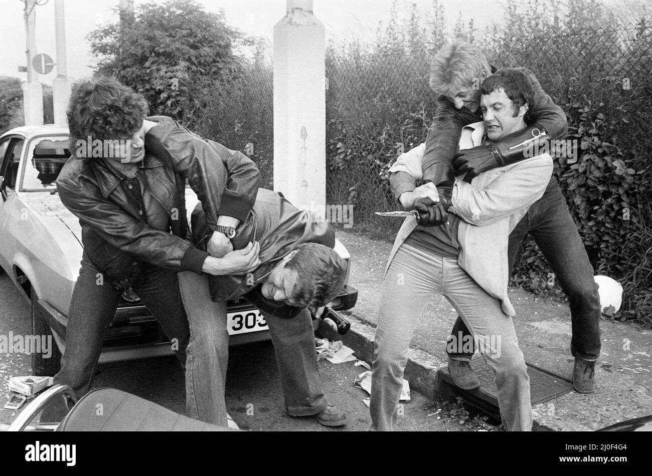 Martin Shaw and Lewis Collins  wrestling with the bad guys on the set of the television Detective series The Professionals.  In the background is their Ford Capri with window smashed out. June 1979. Stock Photo