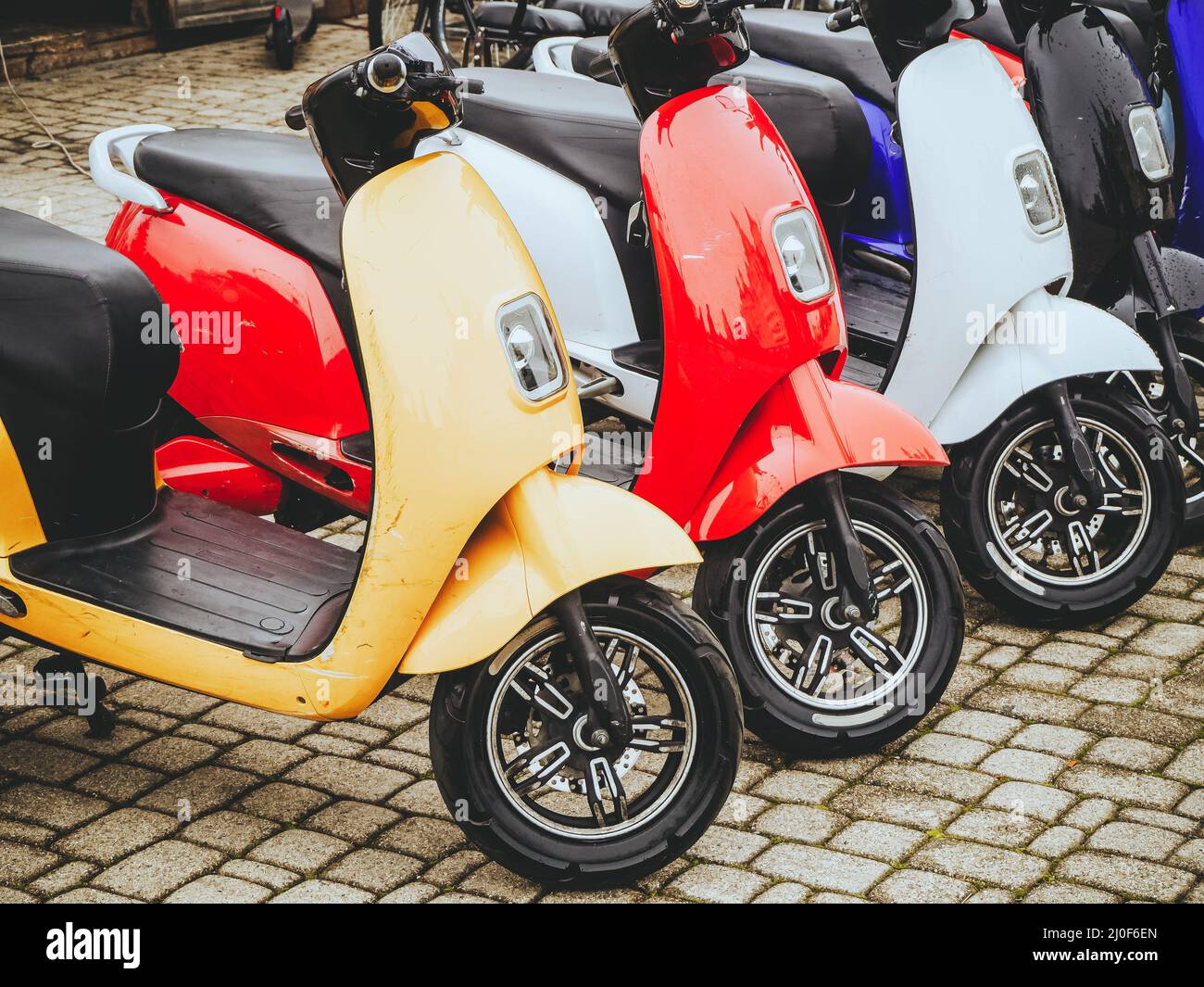 Electric motorcycles of different colors stand in a row on a stone paving slab. Stock Photo