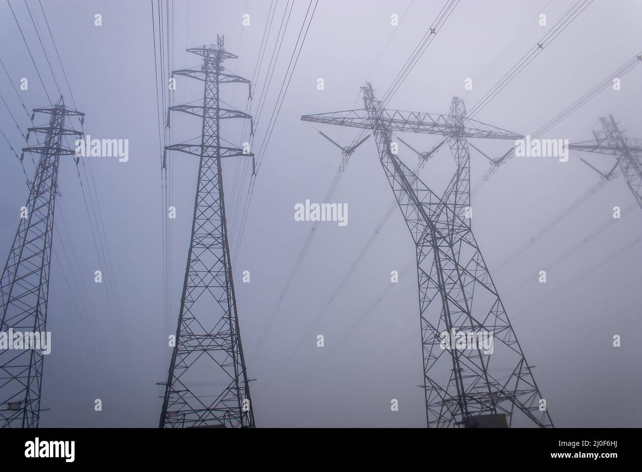 Towering electrical power pylons disappearing into thick fog landscape Stock Photo