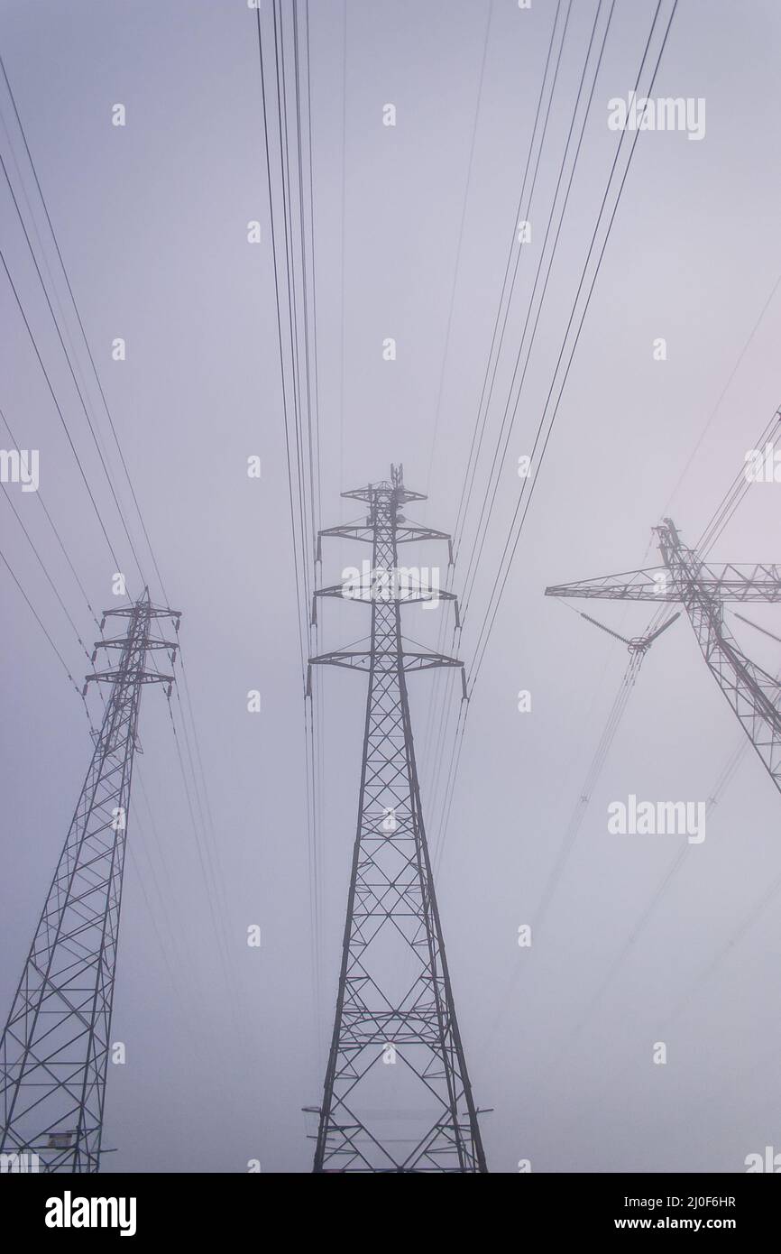 Towering electrical power pylons disappearing into thick fog portrait Stock Photo