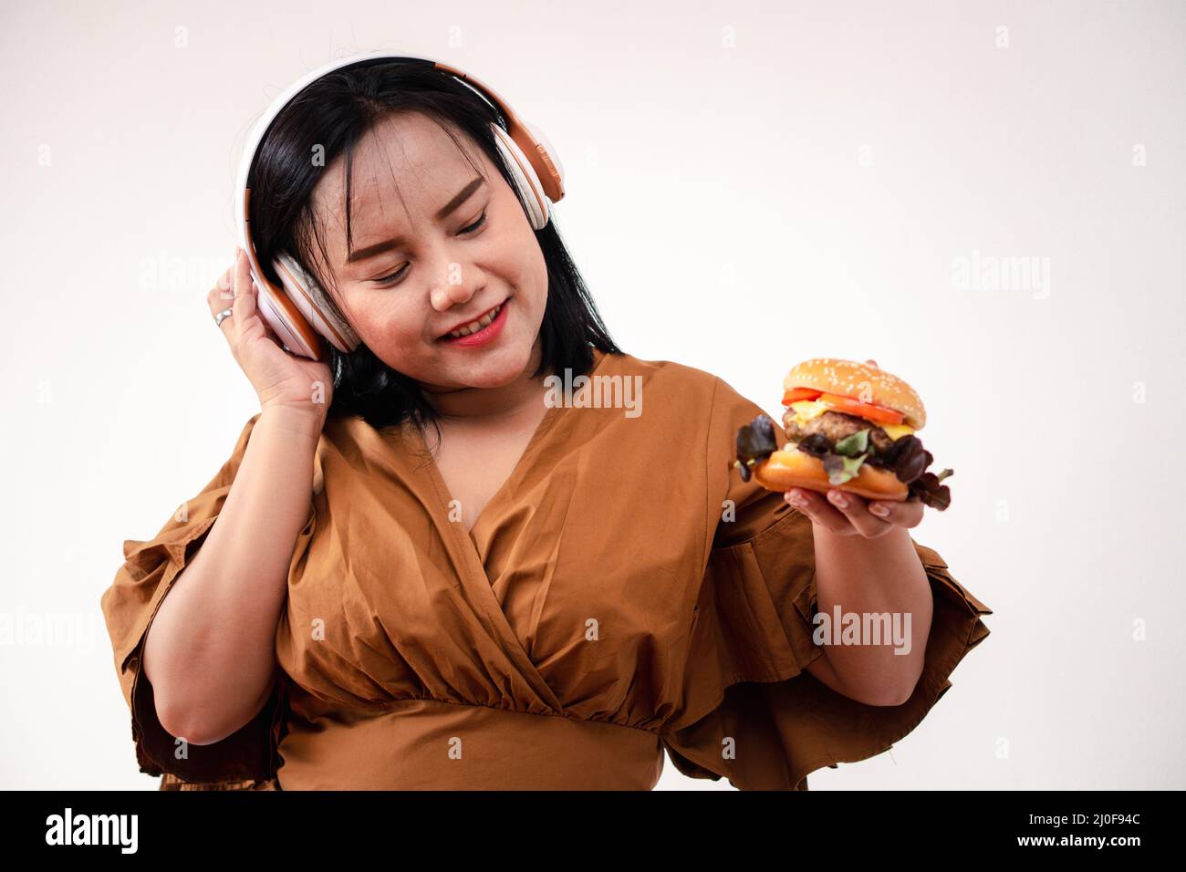 Hungry overweight woman holding hamburger on wooden plate after delivery man delivers foods at home. Concept of binge eating disorder (BED) and Relaxi Stock Photo