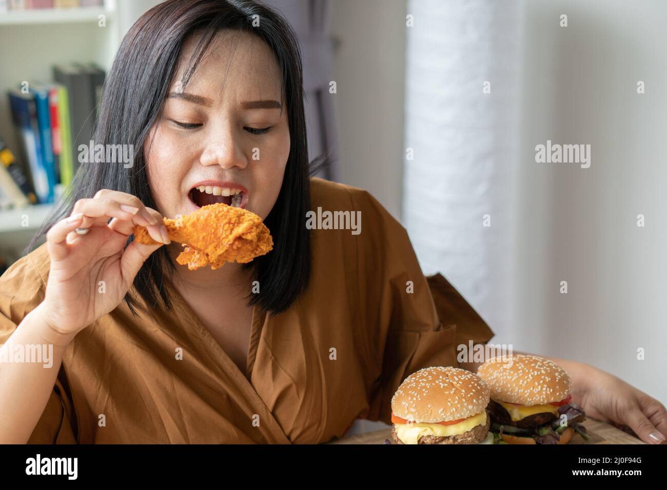 Hungry overweight woman holding Fried Chicken, hamburger on a wooden