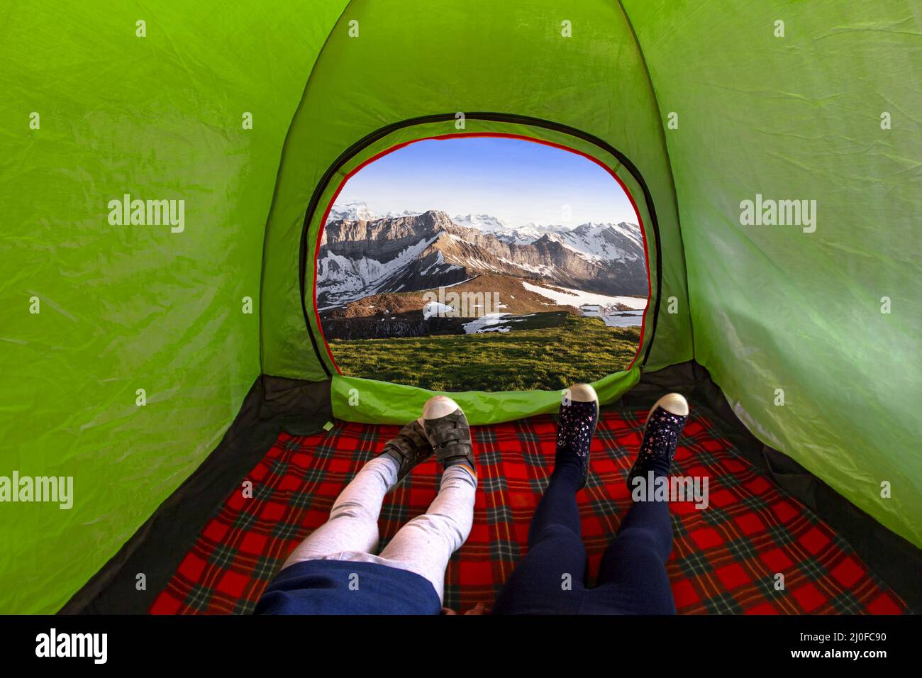 Two kids inside on a camping tent looking at the mountains during the day Stock Photo