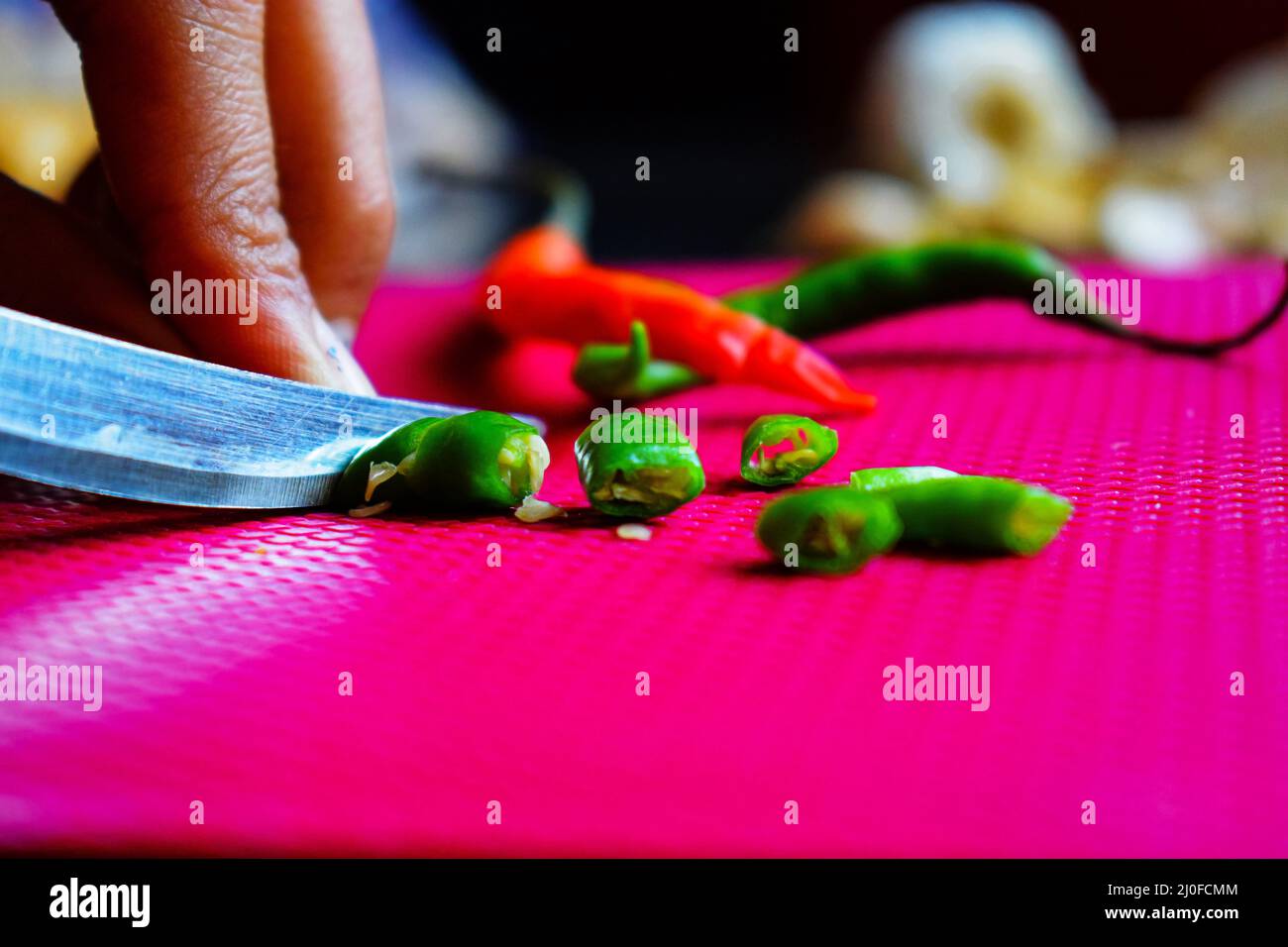 Girl slicing fresh green chili on a dark pink chopping board in the