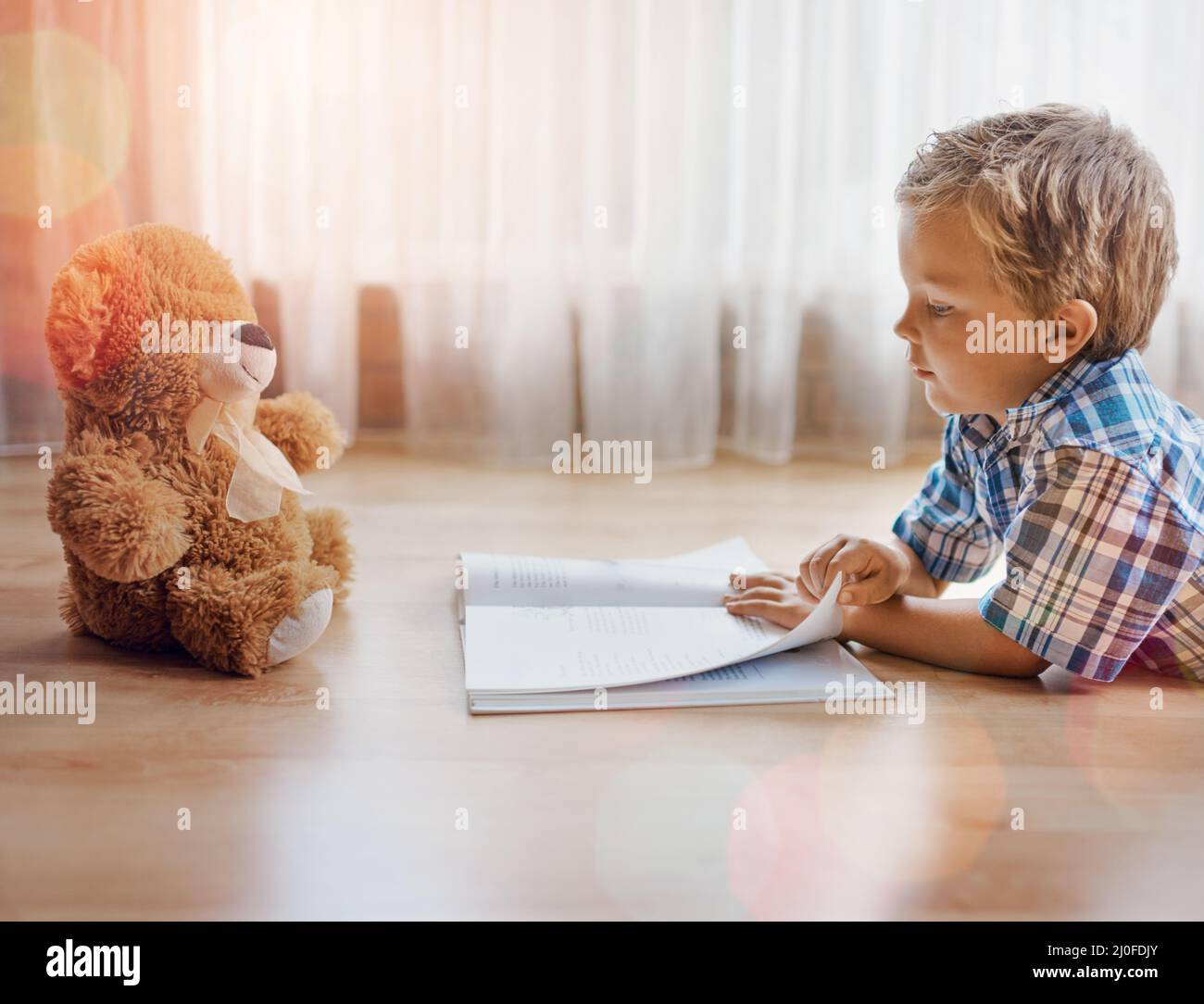 I want to tell you a story.... Shot of a little boy lying on the floor with a book and his teddybear. Stock Photo