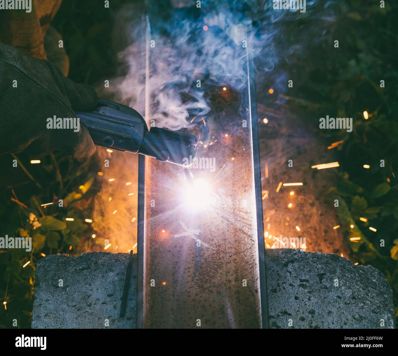 Working man welder burns through an electrode hole in a steel channel in the evening Stock Photo