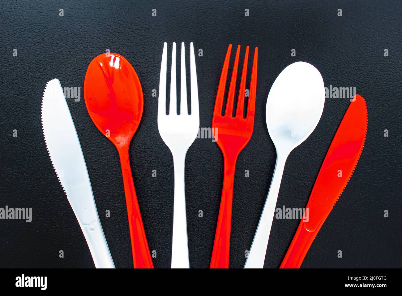 Single use red and white plastic cutlery on a leather background