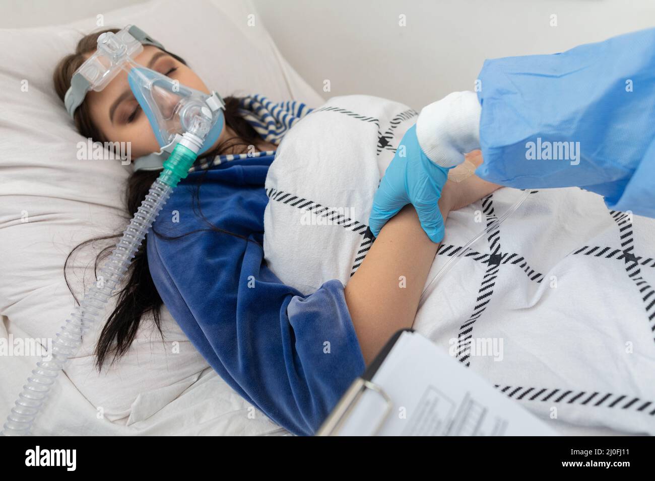 The attending doctor checks the pulse on the wrist of a young teenager lying on a hospital bed. Stock Photo