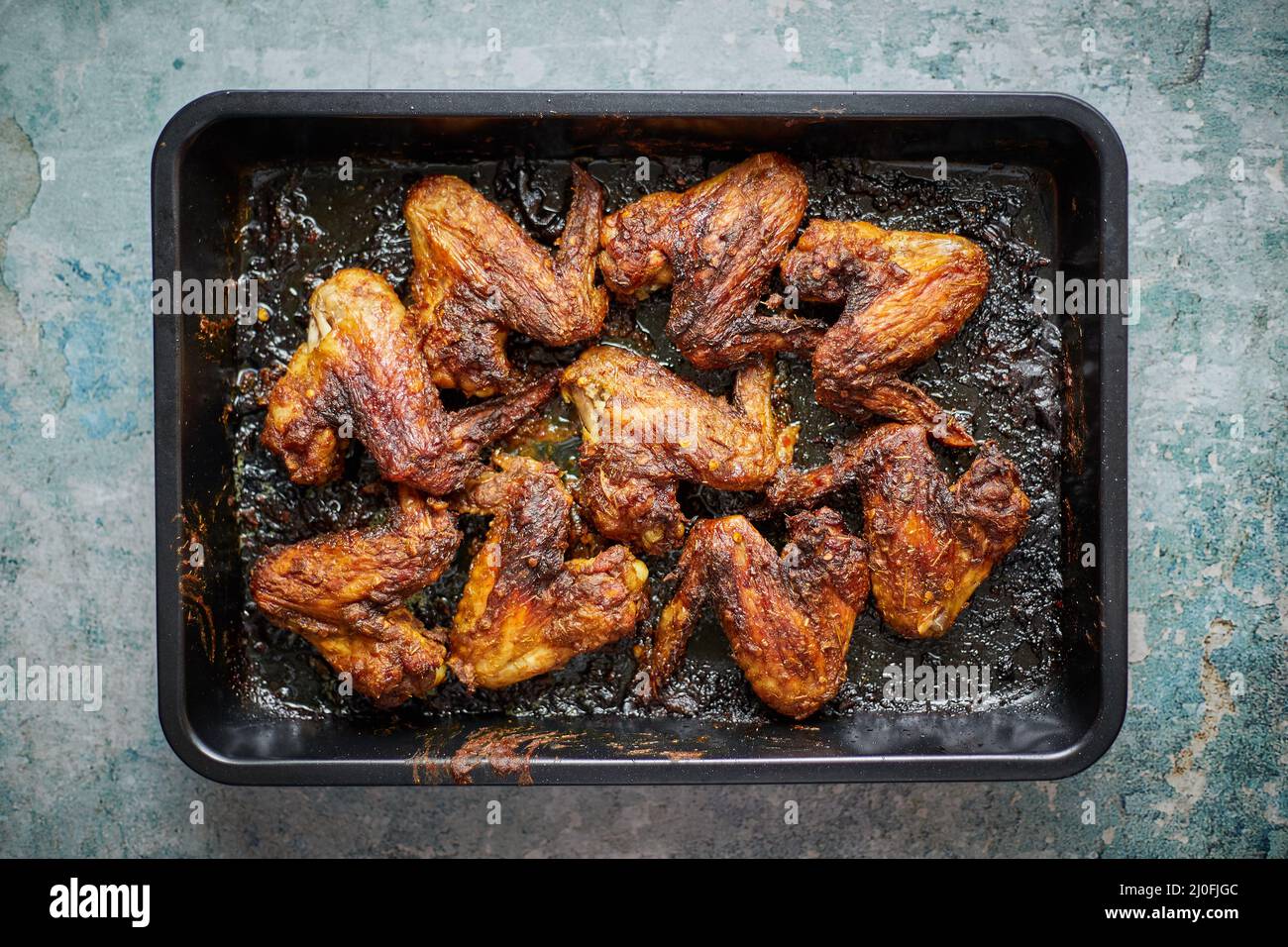 Grilled chicken wings in spices in black metal baking tray on stone