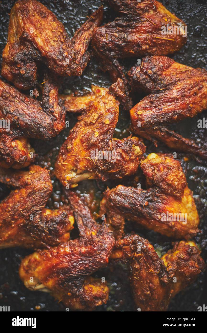 Grilled chicken wings in spices in black metal baking tray on stone