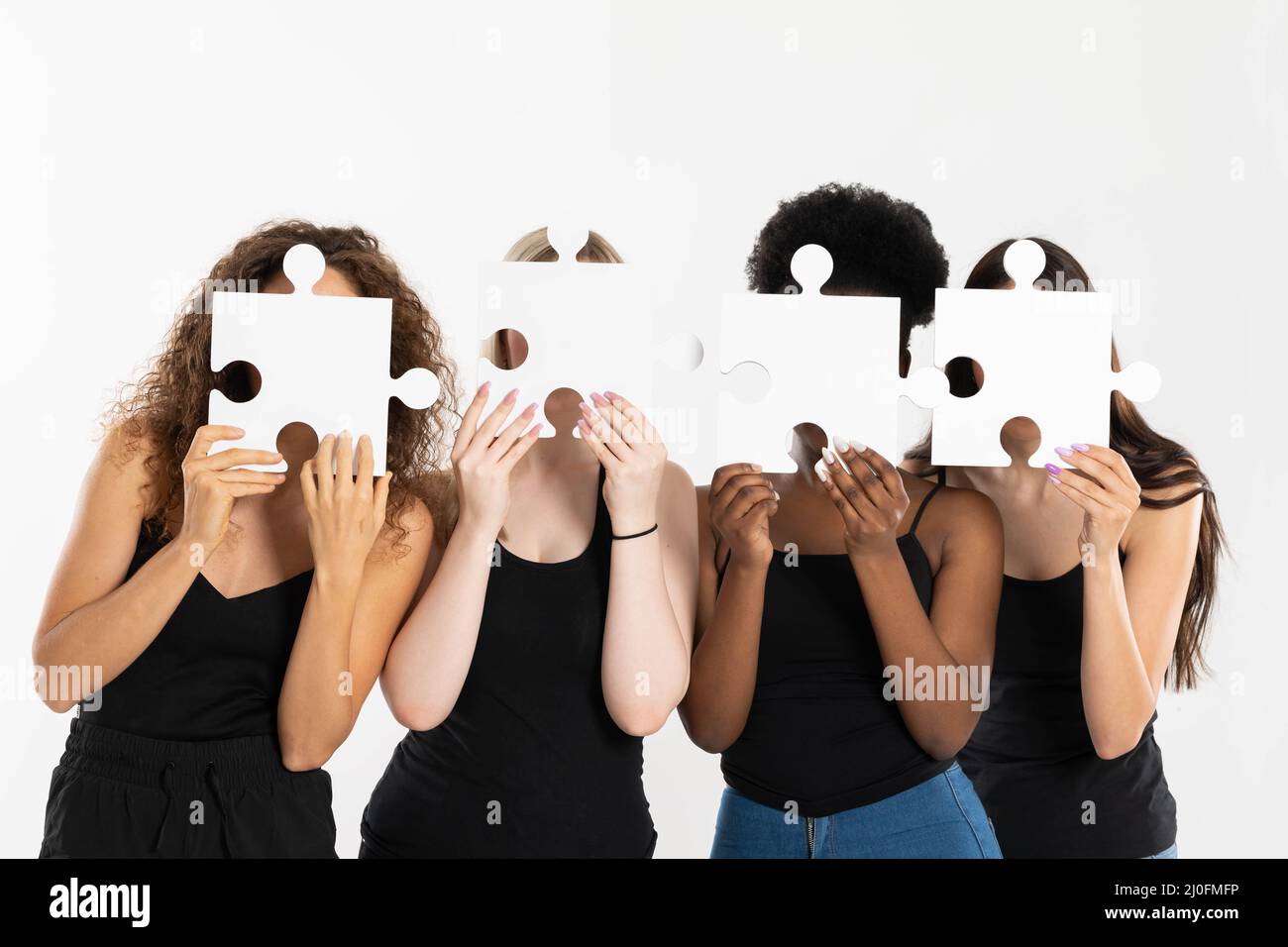 Four young girls are holding puzzles in their hands, covering their face to become anonymous and show that differences connect, Stock Photo