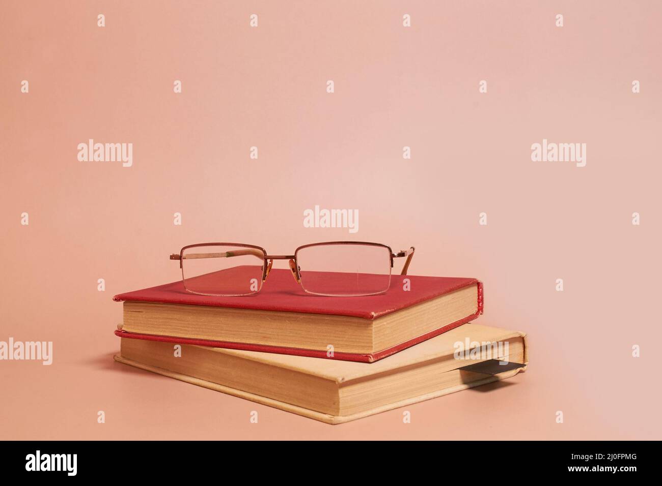 Reading glasses lie on a stack of old worn books on a colored background Stock Photo
