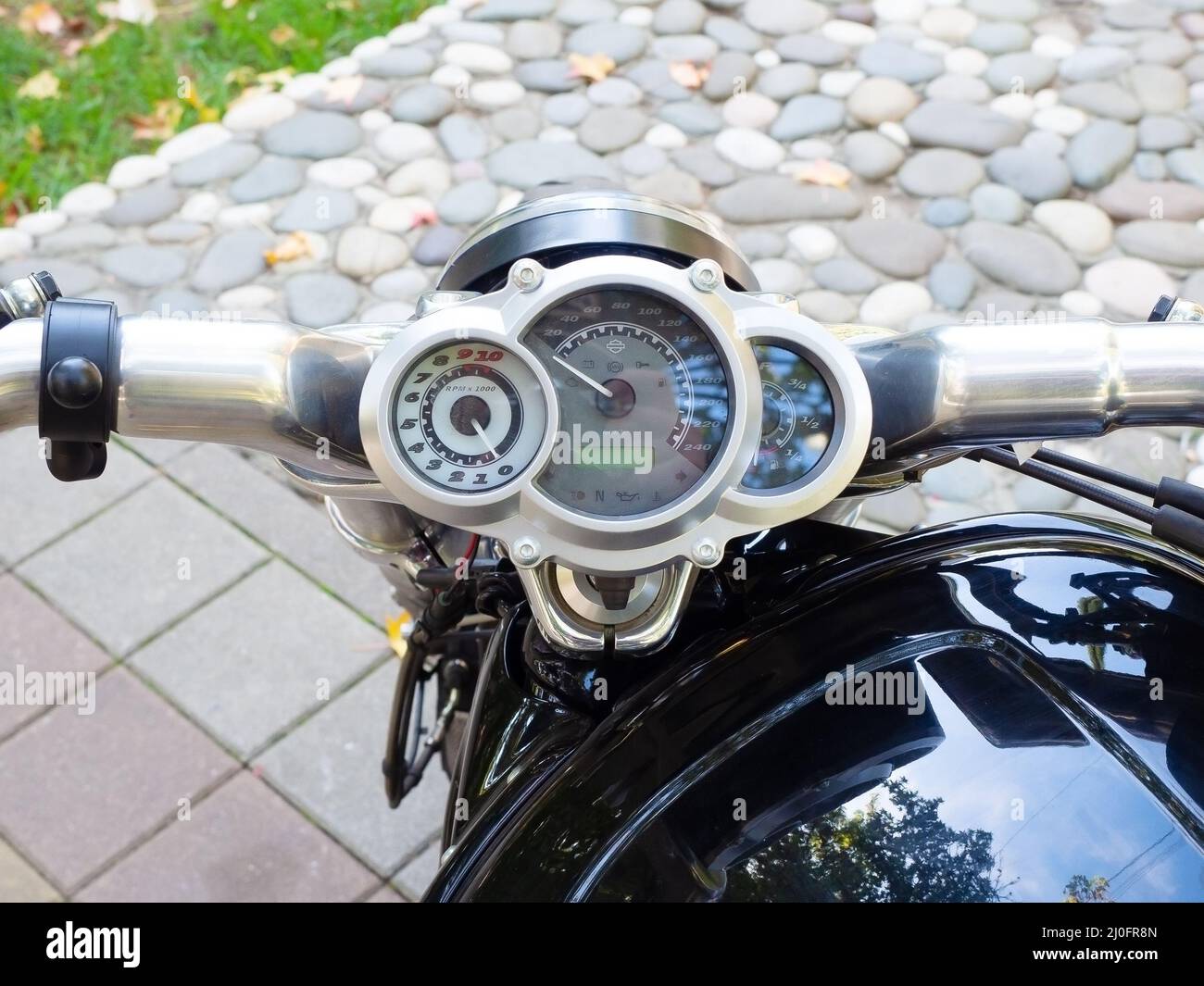 Motorcycle handlebar with circular speedometer against the background of paving slabs and decorative masonry Stock Photo