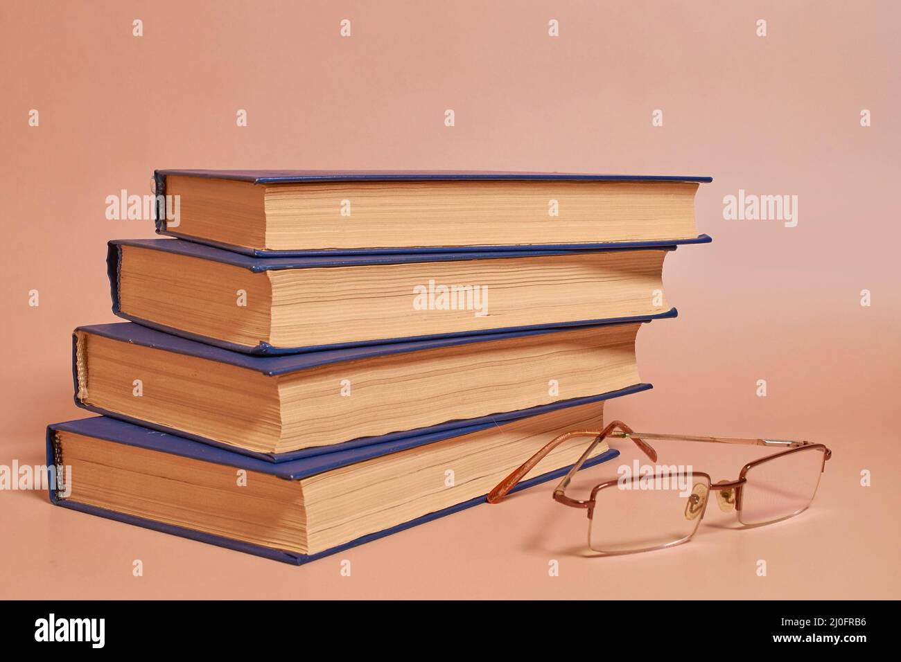Reading glasses lie next to a stack of books on a colored background. Side view Stock Photo