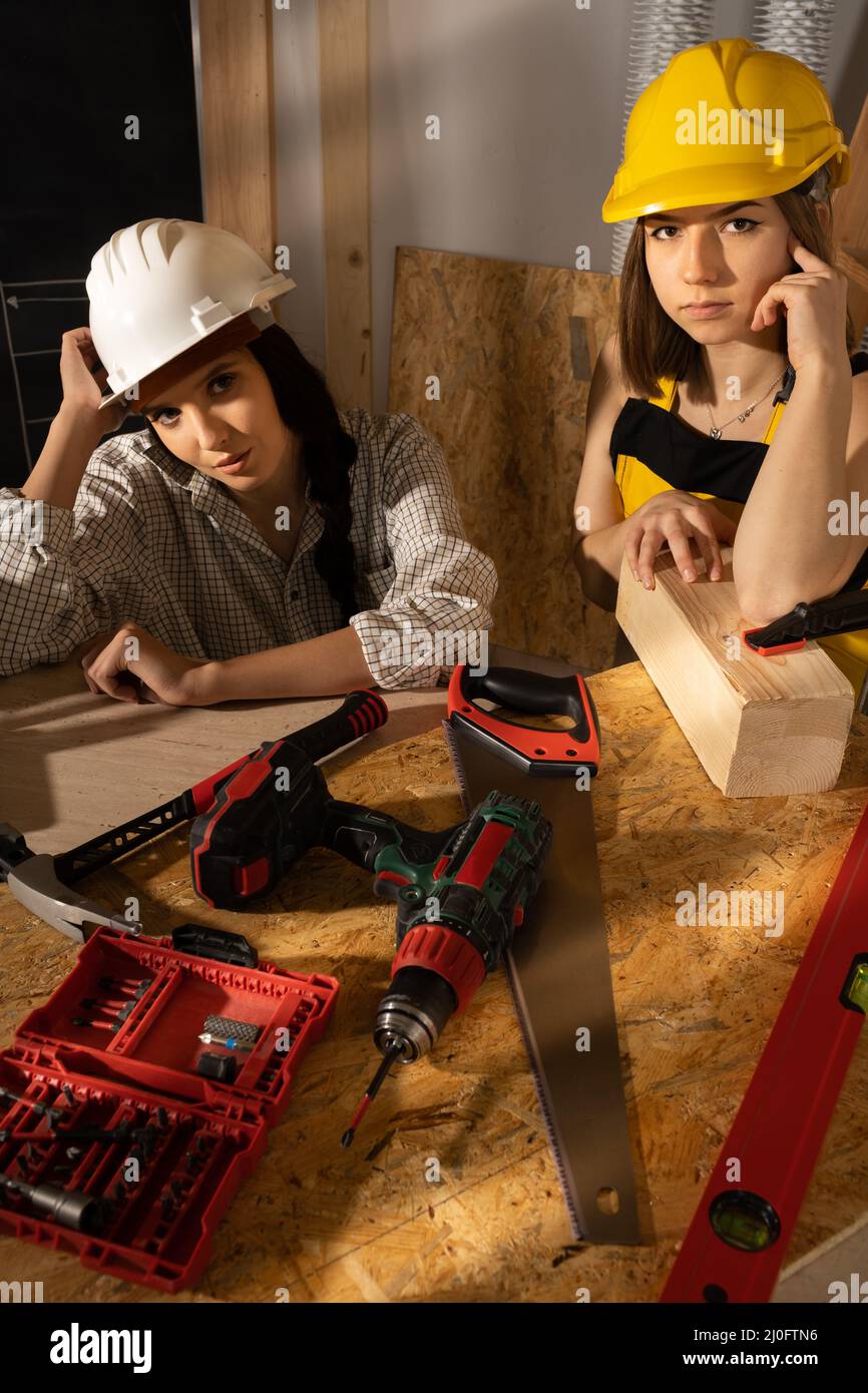 Two girls in working clothes are sitting tired after hard work on a construction site. Blonde and dark haired girls at the const Stock Photo