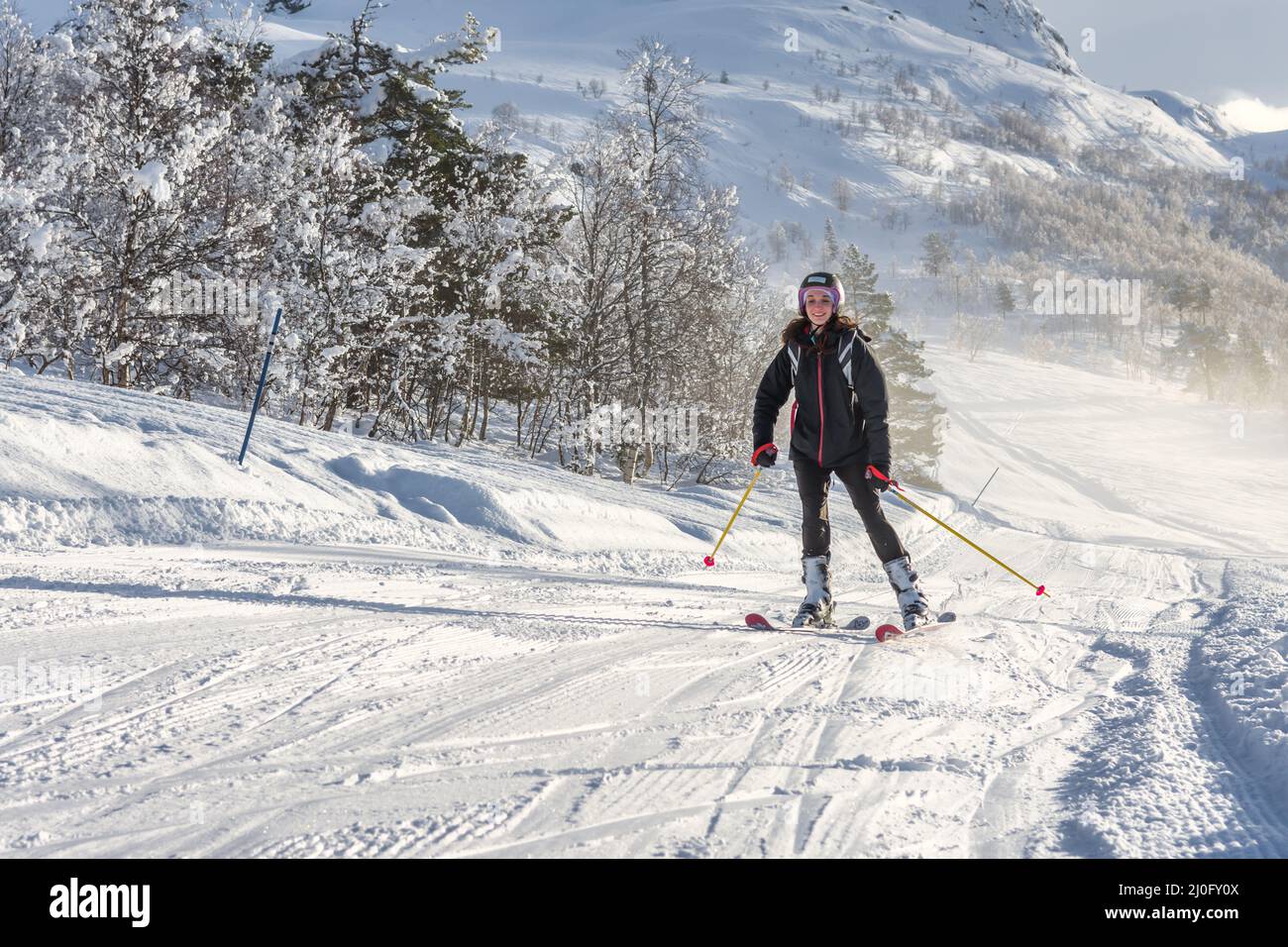 Woman with brown hair smiling, wearing ski wear and a backpack skiing